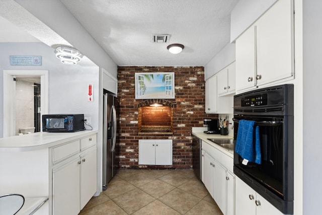 kitchen featuring white cabinets, light tile patterned floors, a textured ceiling, and black appliances