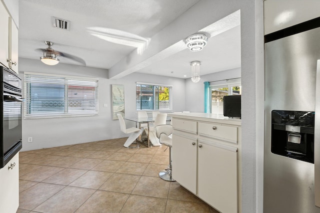 kitchen with pendant lighting, black oven, a textured ceiling, white cabinets, and light tile patterned flooring