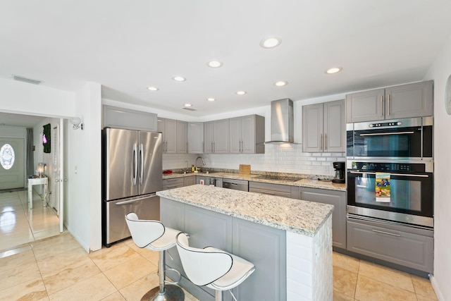 kitchen featuring appliances with stainless steel finishes, tasteful backsplash, a center island, light stone countertops, and wall chimney range hood