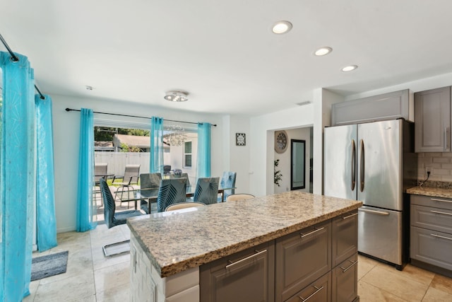 kitchen with a kitchen island, stainless steel fridge, decorative backsplash, light tile patterned floors, and light stone counters