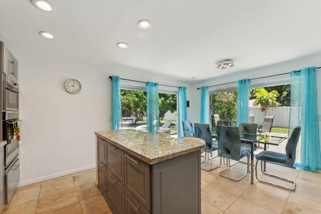 kitchen featuring light stone counters, light tile patterned flooring, a center island, and double oven