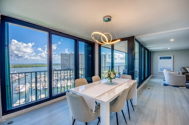 dining room with a water view, a wall of windows, an inviting chandelier, and light wood-type flooring