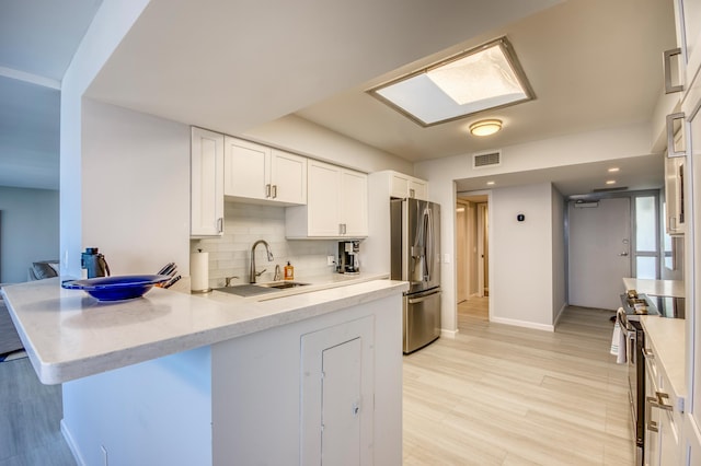 kitchen with sink, kitchen peninsula, white cabinets, stainless steel appliances, and backsplash