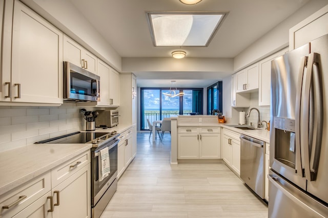 kitchen featuring sink, appliances with stainless steel finishes, white cabinetry, hanging light fixtures, and kitchen peninsula