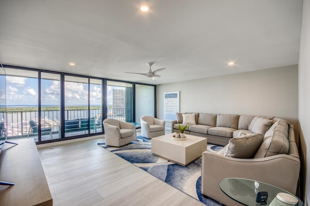 living room featuring expansive windows, a water view, ceiling fan, and light wood-type flooring