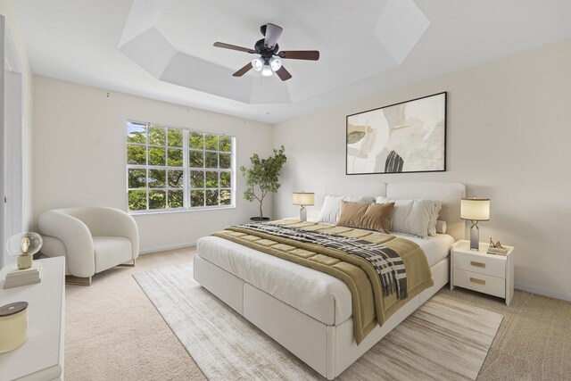 bedroom with light carpet, ceiling fan, and a tray ceiling