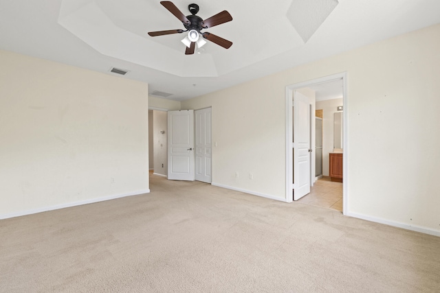 unfurnished bedroom with ceiling fan, light colored carpet, ensuite bath, and a tray ceiling