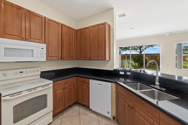 kitchen featuring sink, white appliances, light tile patterned floors, and dark stone counters