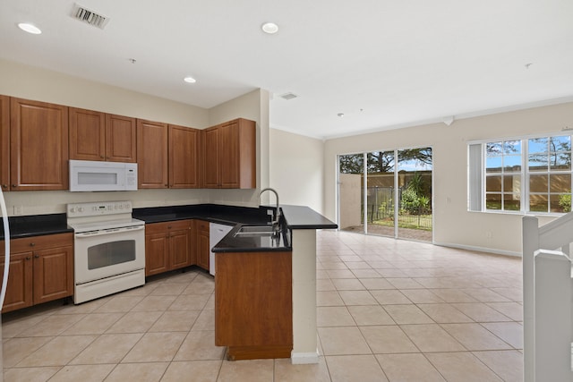 kitchen featuring sink, light tile patterned floors, white appliances, and kitchen peninsula