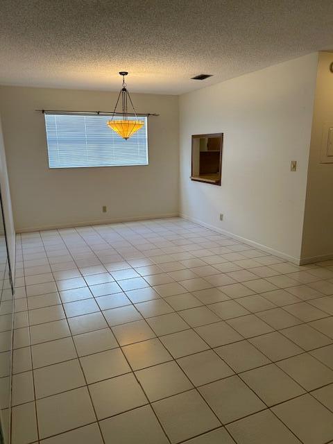 empty room with light tile patterned floors, a textured ceiling, and a healthy amount of sunlight