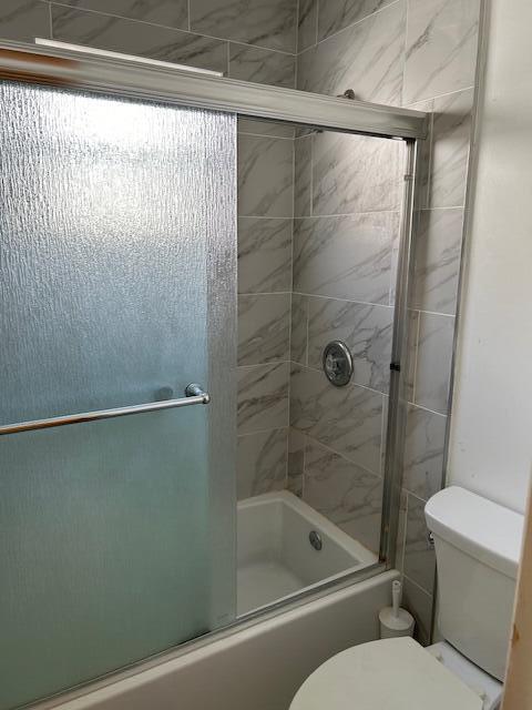 bathroom with combined bath / shower with glass door and toilet