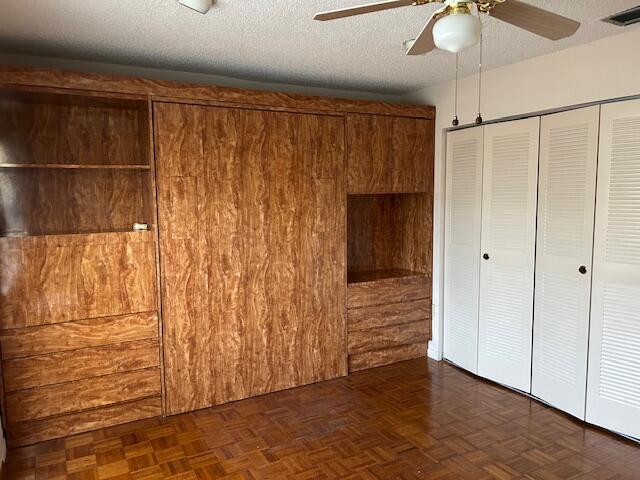 unfurnished bedroom featuring ceiling fan, dark parquet floors, a closet, and a textured ceiling