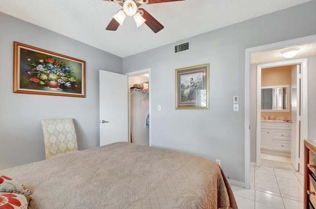 bedroom featuring sink, a walk in closet, a textured ceiling, light tile patterned floors, and ceiling fan