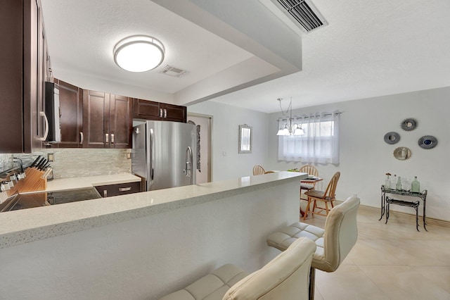 kitchen featuring decorative light fixtures, tasteful backsplash, stainless steel fridge, light stone countertops, and a textured ceiling