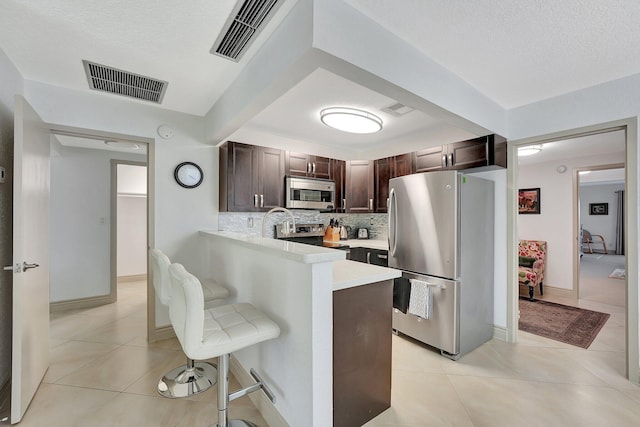 kitchen featuring light tile patterned floors, backsplash, a kitchen breakfast bar, stainless steel appliances, and kitchen peninsula