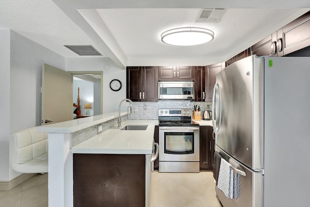 kitchen with light tile patterned flooring, dark brown cabinetry, sink, kitchen peninsula, and stainless steel appliances