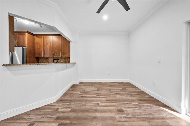 kitchen with ornamental molding, stainless steel fridge, hardwood / wood-style flooring, light stone countertops, and backsplash