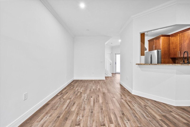 unfurnished living room with sink, crown molding, and light hardwood / wood-style flooring