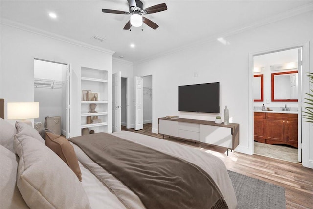 bedroom with connected bathroom, sink, a spacious closet, crown molding, and light wood-type flooring