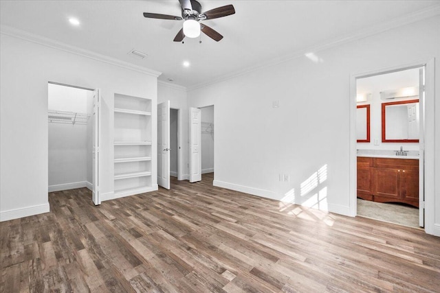 unfurnished bedroom featuring sink, crown molding, hardwood / wood-style floors, connected bathroom, and multiple closets