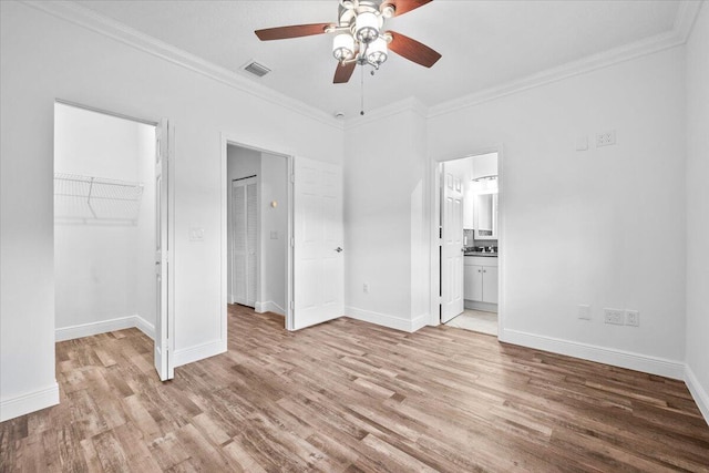 unfurnished bedroom featuring ornamental molding, a walk in closet, connected bathroom, and light hardwood / wood-style flooring