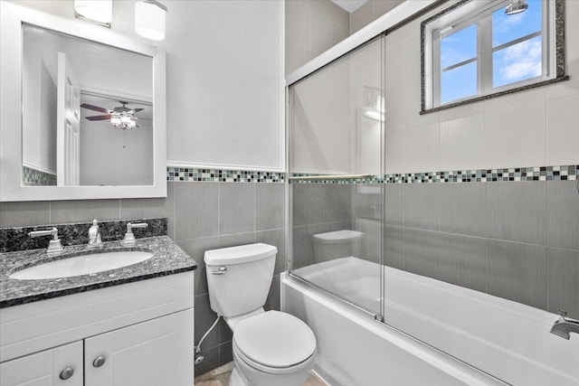 full bathroom featuring tile walls, shower / bath combination with glass door, vanity, ceiling fan, and toilet