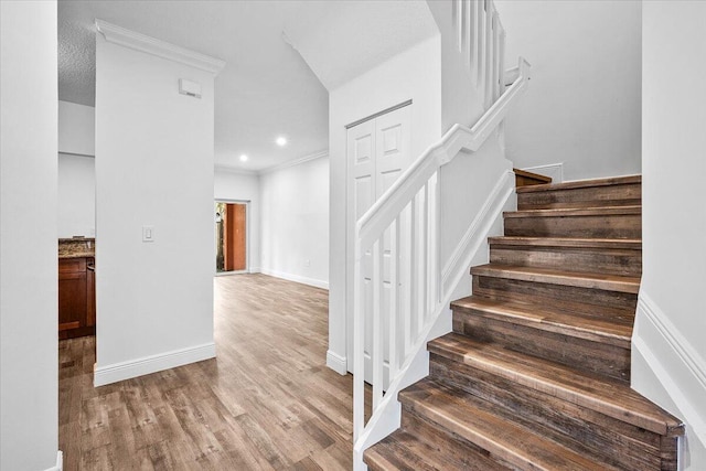 staircase with wood-type flooring and crown molding