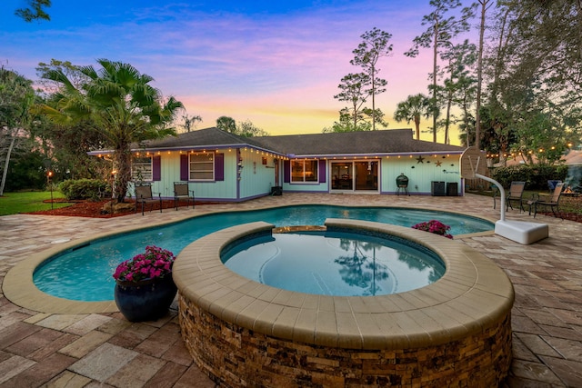 pool at dusk featuring an in ground hot tub and a patio area