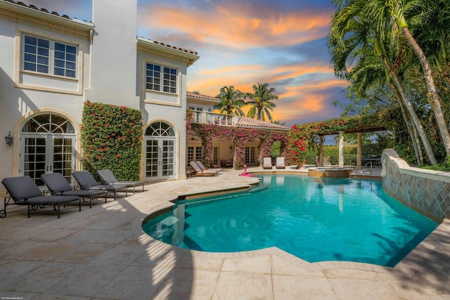 pool at dusk featuring french doors, an in ground hot tub, and a patio area