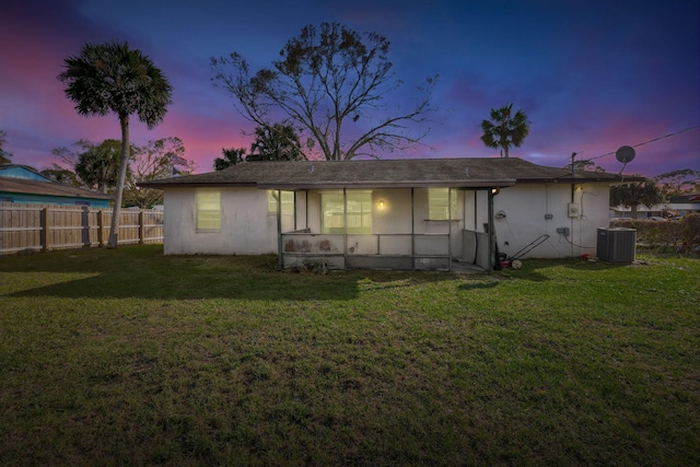 back house at dusk with central AC unit and a yard