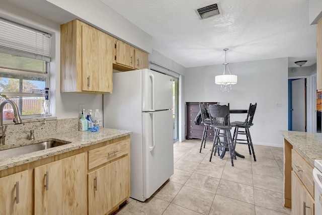 kitchen featuring sink, a textured ceiling, light brown cabinetry, decorative light fixtures, and white fridge