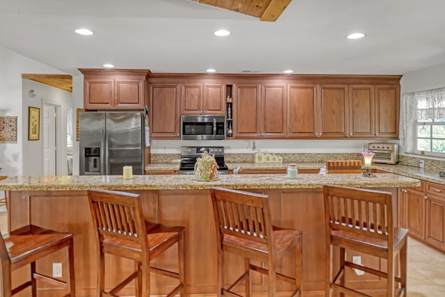 kitchen with a breakfast bar area, light stone counters, light tile patterned floors, a kitchen island, and stainless steel appliances