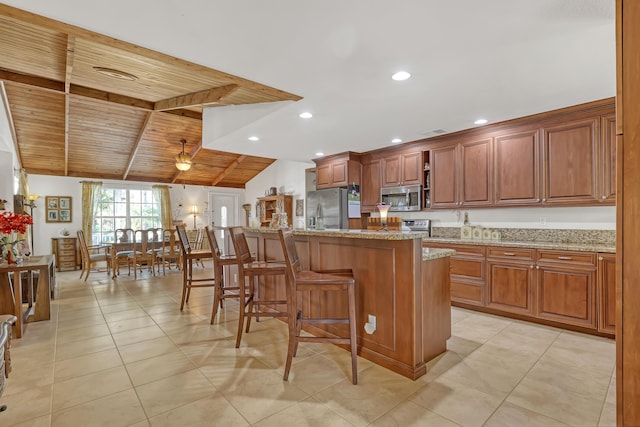 kitchen with a kitchen bar, wooden ceiling, appliances with stainless steel finishes, a kitchen island, and light stone countertops