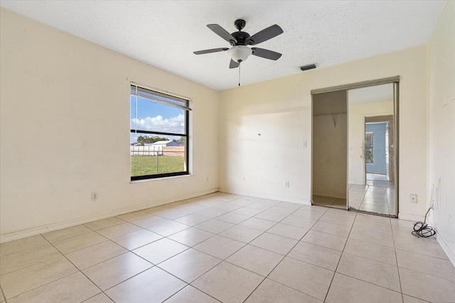 empty room with ceiling fan, a textured ceiling, and light tile patterned floors