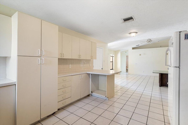 kitchen with white refrigerator, kitchen peninsula, tasteful backsplash, and light tile patterned floors