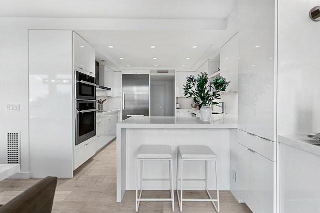 kitchen featuring a breakfast bar area, white cabinetry, kitchen peninsula, built in fridge, and black electric stovetop