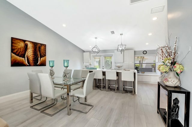 dining area with vaulted ceiling, plenty of natural light, a chandelier, and light hardwood / wood-style floors