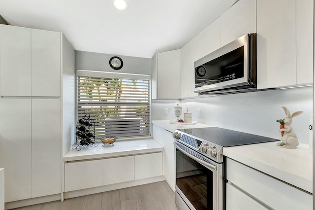 kitchen with stainless steel appliances, white cabinetry, and light wood-type flooring