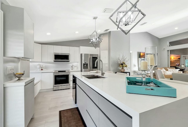 kitchen with an island with sink, sink, white cabinets, hanging light fixtures, and stainless steel appliances