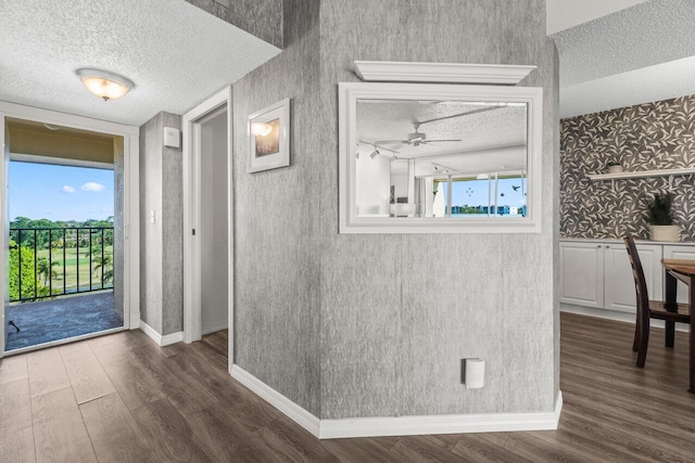 interior space featuring baseboards, dark wood-type flooring, a textured ceiling, and wallpapered walls