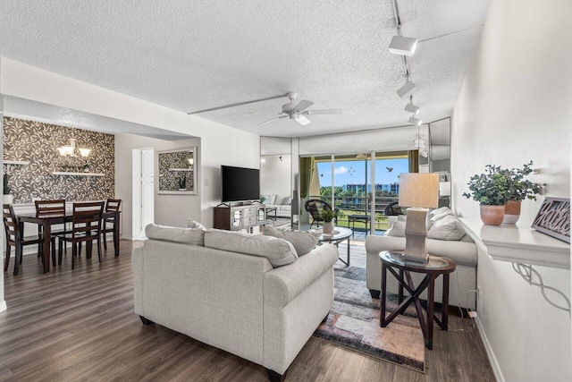 living room with ceiling fan with notable chandelier, dark wood-type flooring, rail lighting, and a textured ceiling