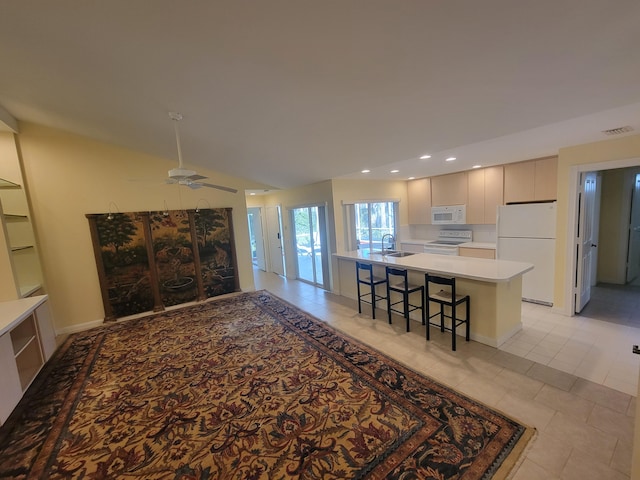 kitchen featuring an island with sink, lofted ceiling, sink, a breakfast bar area, and white appliances