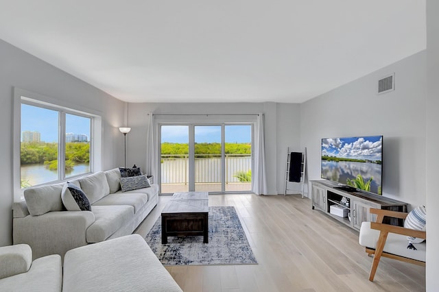 living area featuring a water view, light wood finished floors, and visible vents