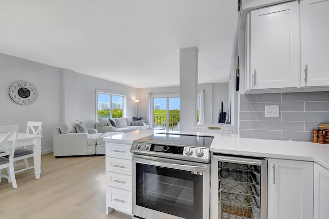 kitchen featuring electric stove, wine cooler, open floor plan, light countertops, and white cabinetry