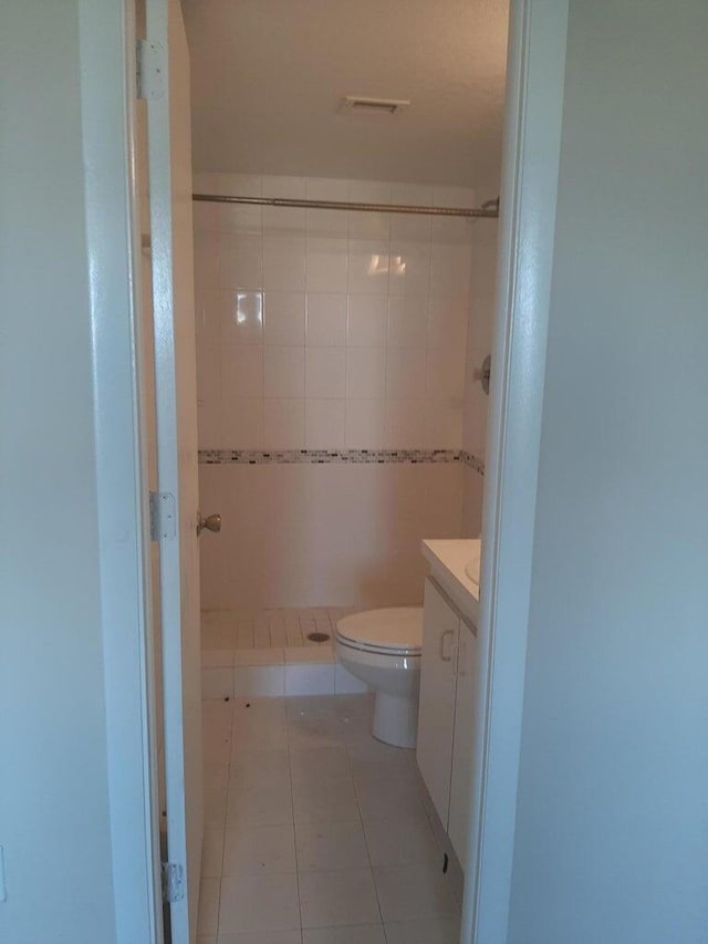 bathroom with tile patterned flooring, vanity, toilet, and tiled shower