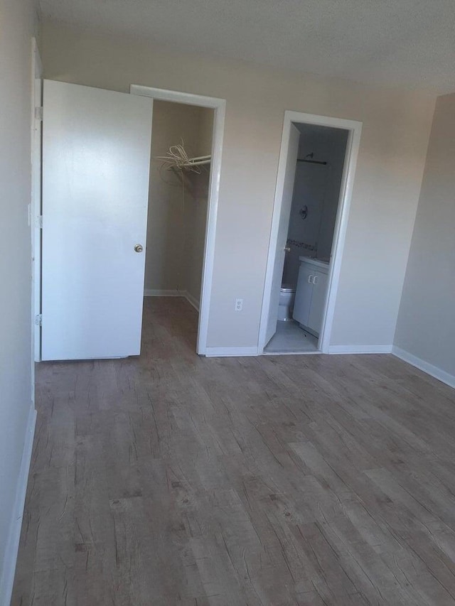 unfurnished bedroom with hardwood / wood-style flooring, a walk in closet, a closet, and ensuite bathroom