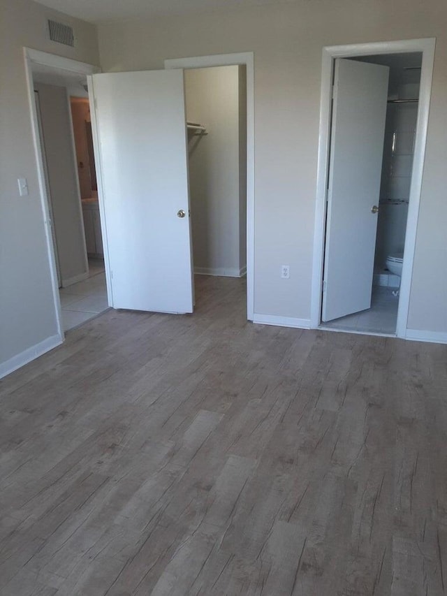 unfurnished bedroom with ensuite bathroom, a spacious closet, light hardwood / wood-style floors, and a closet