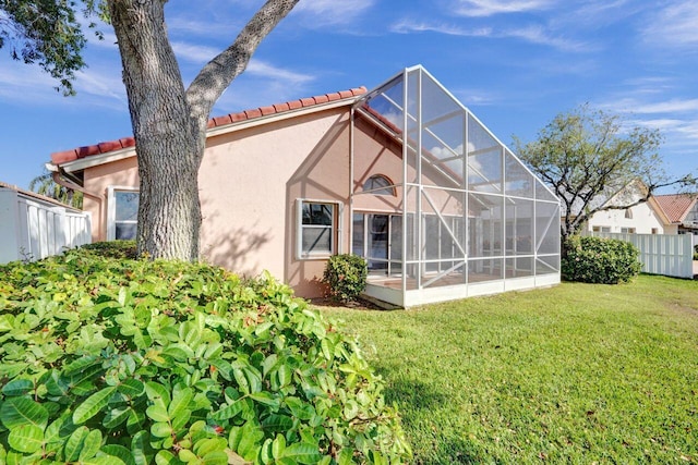 back of property with stucco siding, a tiled roof, a yard, and fence