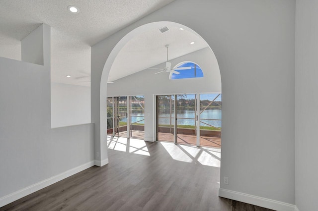 interior space with lofted ceiling, a water view, a textured ceiling, dark hardwood / wood-style flooring, and ceiling fan