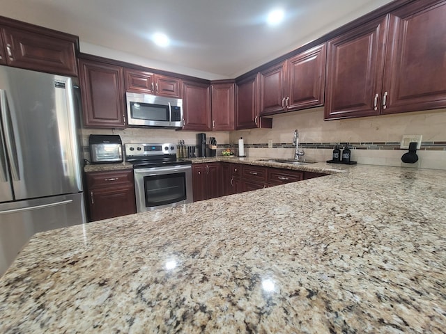 kitchen featuring appliances with stainless steel finishes, light stone countertops, sink, and backsplash